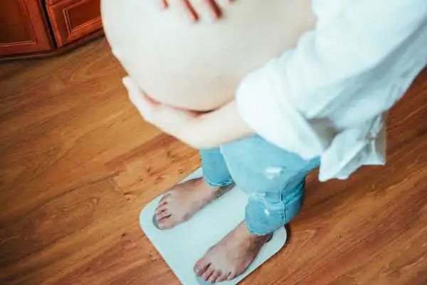 Image of woman weighing herself and experiencing weight gain through pregnancy Stirling